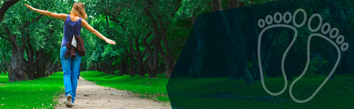 Podologie Header: Eine blau gekleidete Frau ist von hinten auf einem Feldweg zu sehen. Sie scheint zu balancieren.